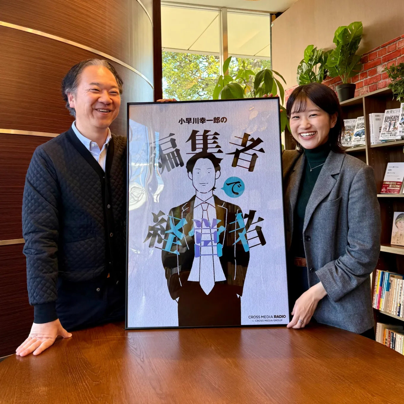小早川さんと広報担当の濱中さん、2周年記念ポスターとの記念写真
